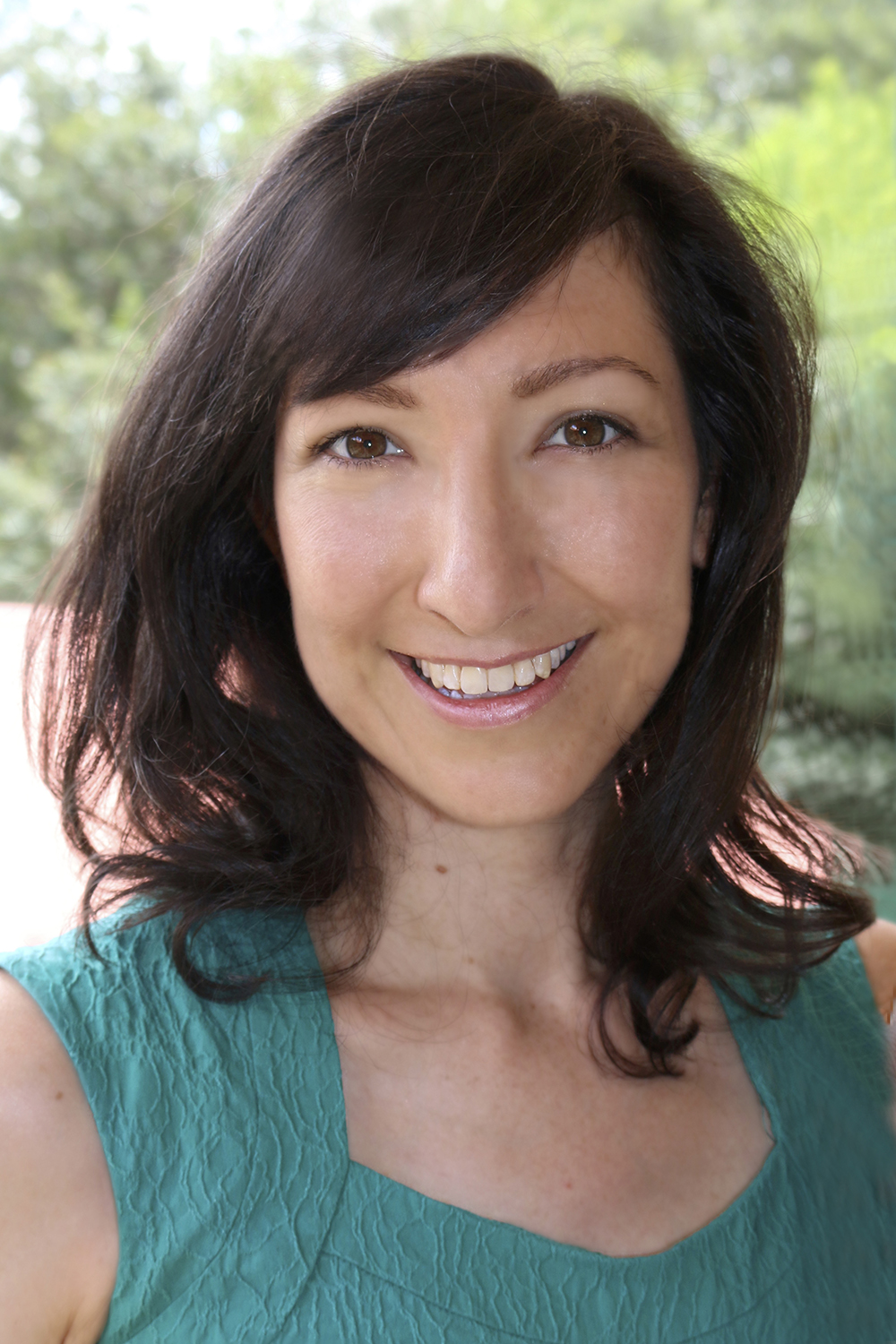 Professional headshot of Hana. She has dark shoulder length hair and is wearing a green top. She is outdoors and smiling. 