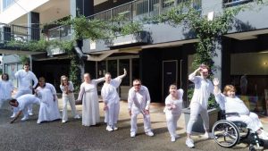 A group of performsers all dressed in white lined up in different poses.