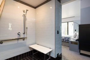 Spicers Retreat New Farms accessible bathroom. The bathroom is white, with black floor tiles. There is a show head connected to raining and additional railing in the shower, along with a seat.