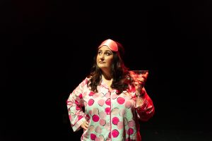 Emma is in pink and white polka dot pyjamas with a pink sleeping mask. She is holding a martini glass and looking upwards.