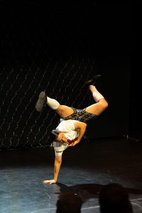 A girl performing on stage doing a one handed handstand.