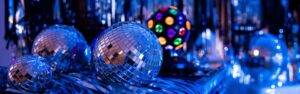 A image of multiple disco balls in various sizes and a disco light sitting on a table of blue, silver streamers.