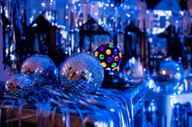A image of multiple disco balls in various sizes and a disco light sitting on a table of blue, silver streamers.