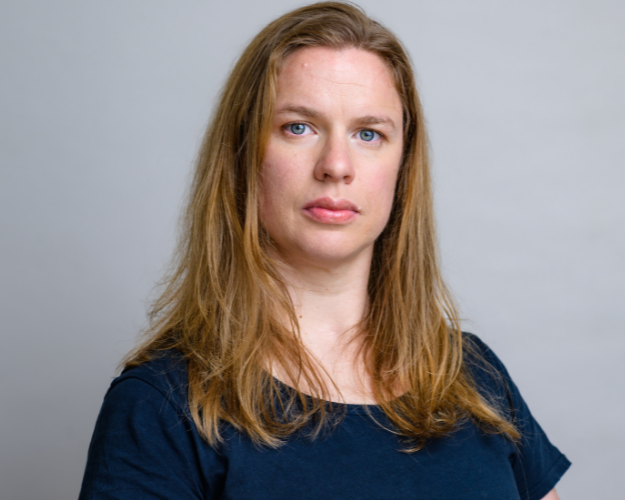 A headshot of Alisha McLennan Marler with long hair and a dark t-shirt poses in front of a gray backdrop. Her expression is neutral and is looking directly at the camera.