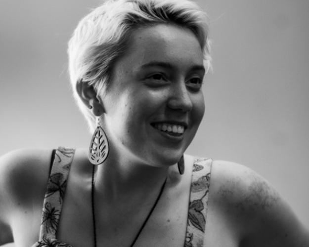 A headshot of India Rose smiling and looking away from the camera. The photo is black and white. India has short light hair and is wearing large earrings.
